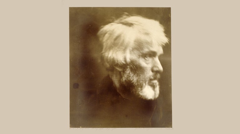 A faded sepia toned photograph of a bearded, white haired Thomas Carlyle in profile view